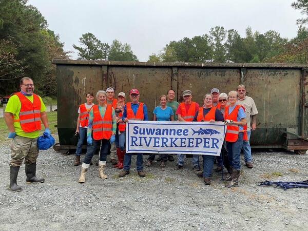 [Suwannee Riverkeeper banner at a Troupville cleanup. Lowndes County Chairman Bill Slaughter is second from right, back row. WWALS E.D. Gretchen Quarterman is by the left end of the banner.]