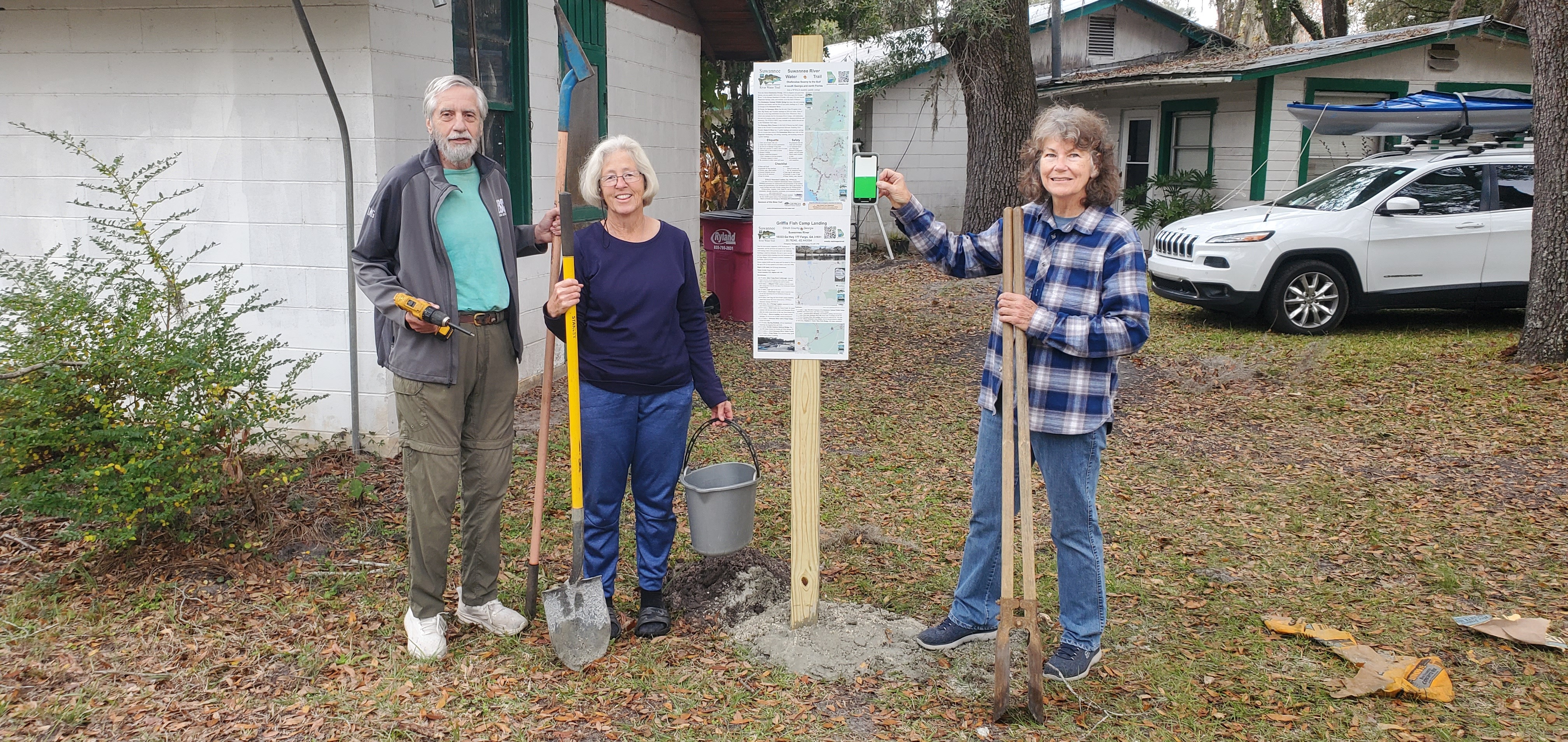 Richard Fowler with digger, Shirley Kokidko with water bucket, Linda Tindall with phone as level at Griffis Fish Camp