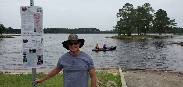 [WLRWT signs, WWALS Trails Committee Chair Dan Phillips, WWALS president Tom H. Johnson Jr. in Suwannee Riverkeeper vessel, Reed Bingham State Park Lake]