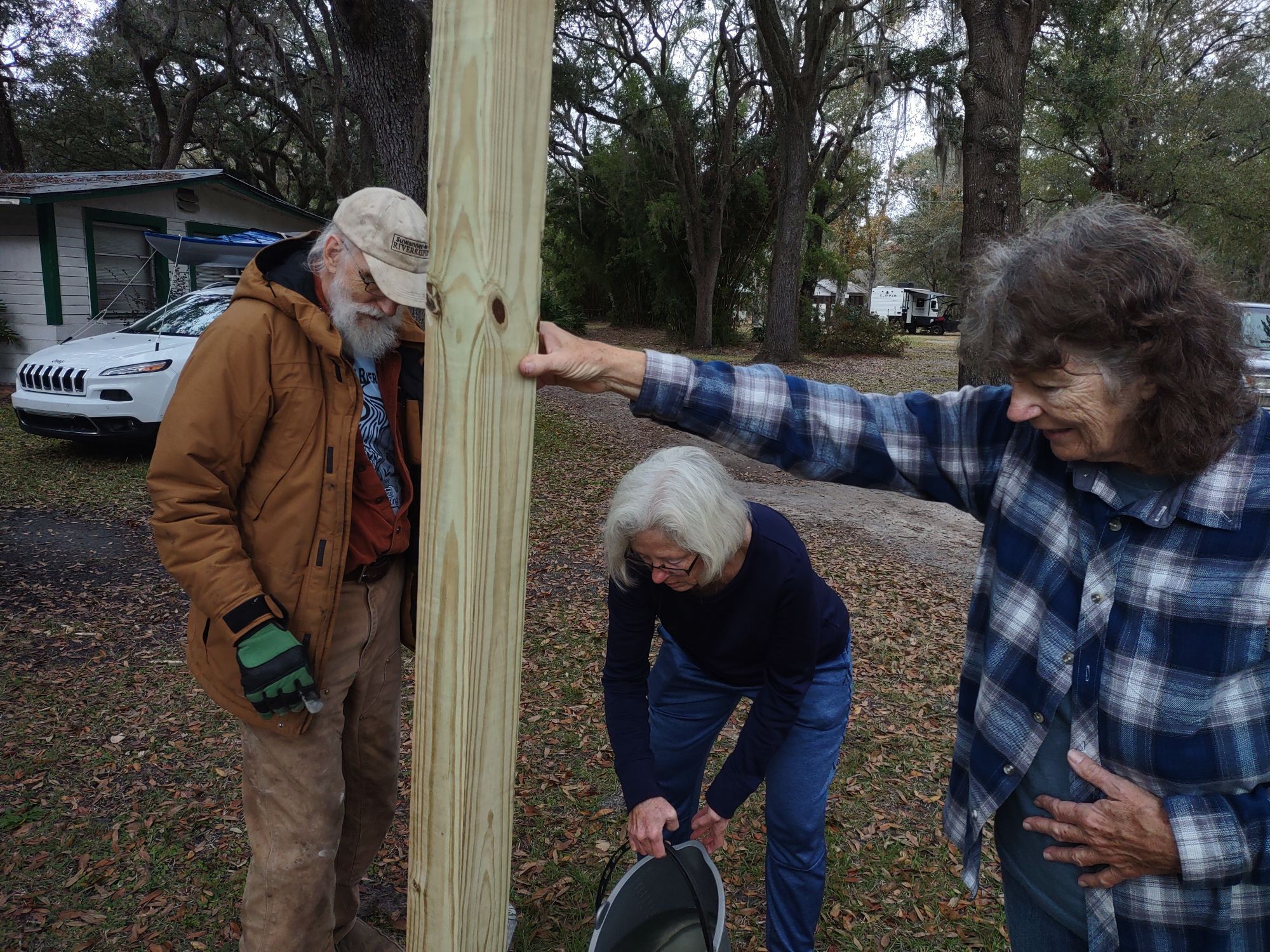 Linda holds the signpost while Shirley pours water on the Quikrete --Richard Fowler