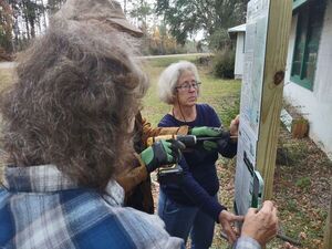 [Shirley holds the bottom sign while Linda levels and jsq screws it onto the signpost --Richard Fowler]